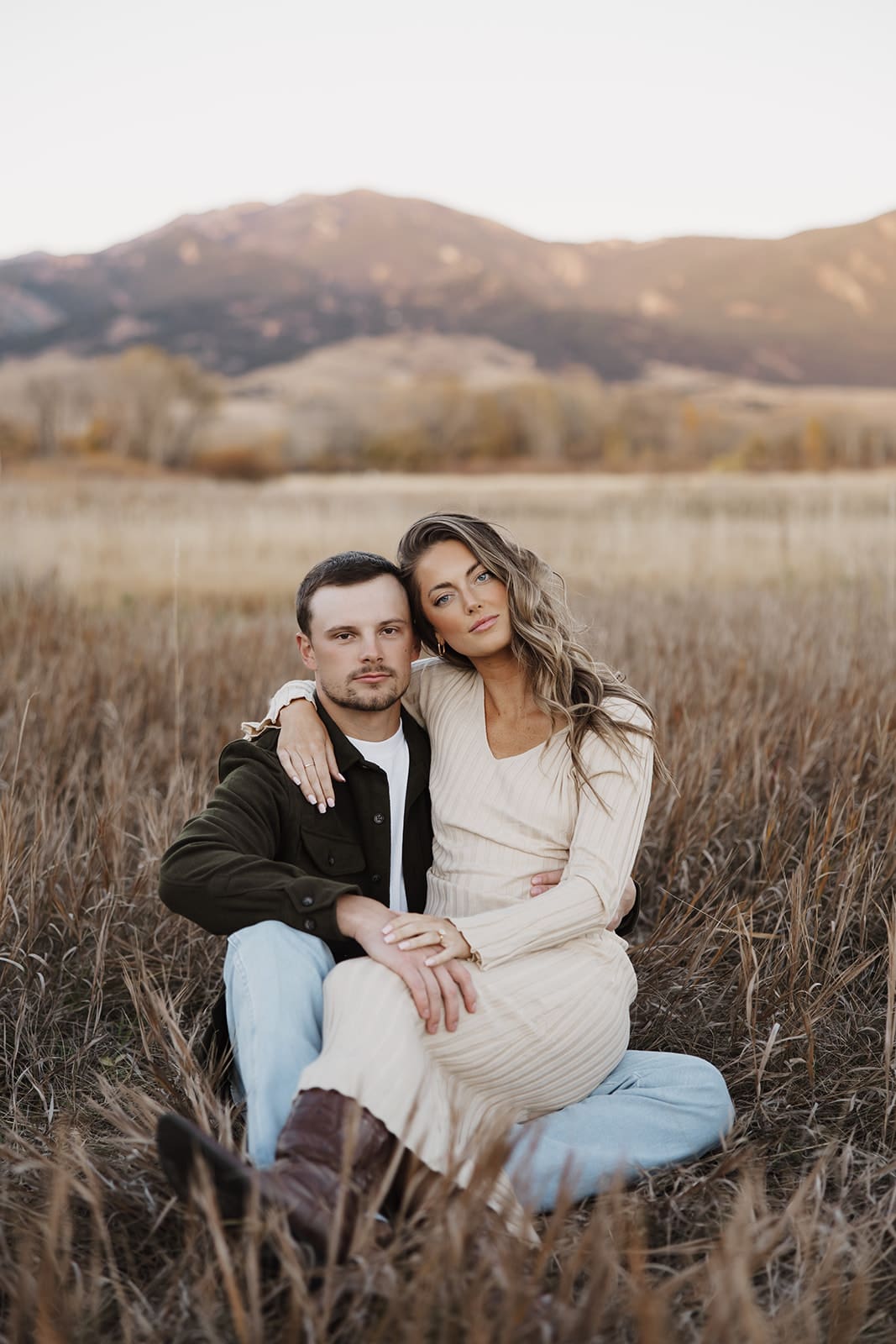 Cute engaged couple posing in a Bozeman, MT field with mountain backdrop