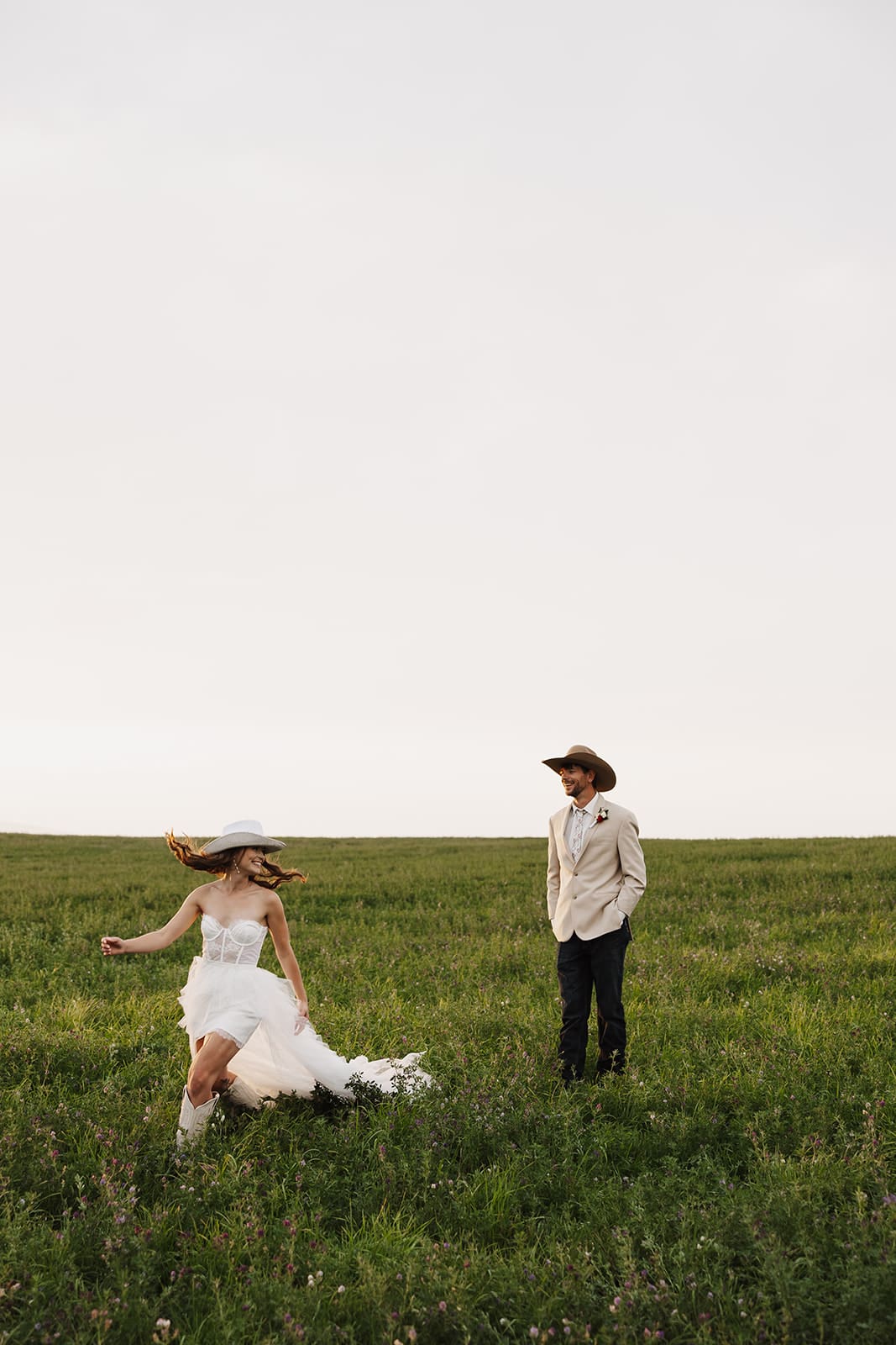 Bride and groom chasing each other in a field during their montana wedding