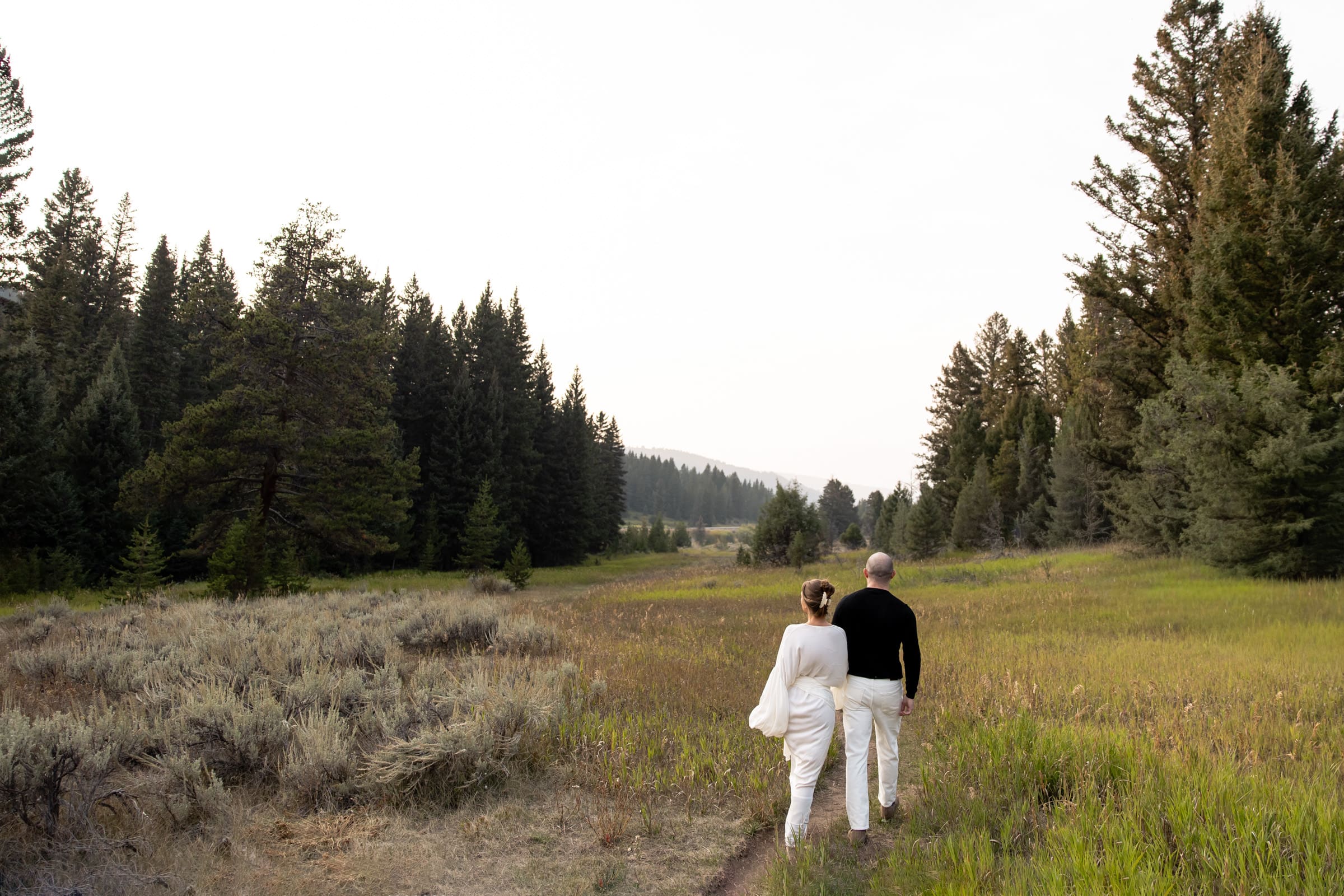 Bride-to-be in an editorial white gown looking at her fiancé in the Montana mountains.