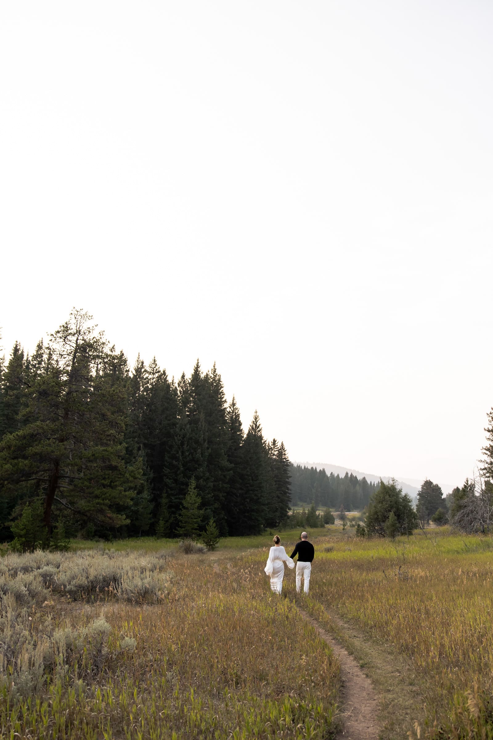 Bride-to-be in an editorial white gown looking at her fiancé in the Montana mountains.