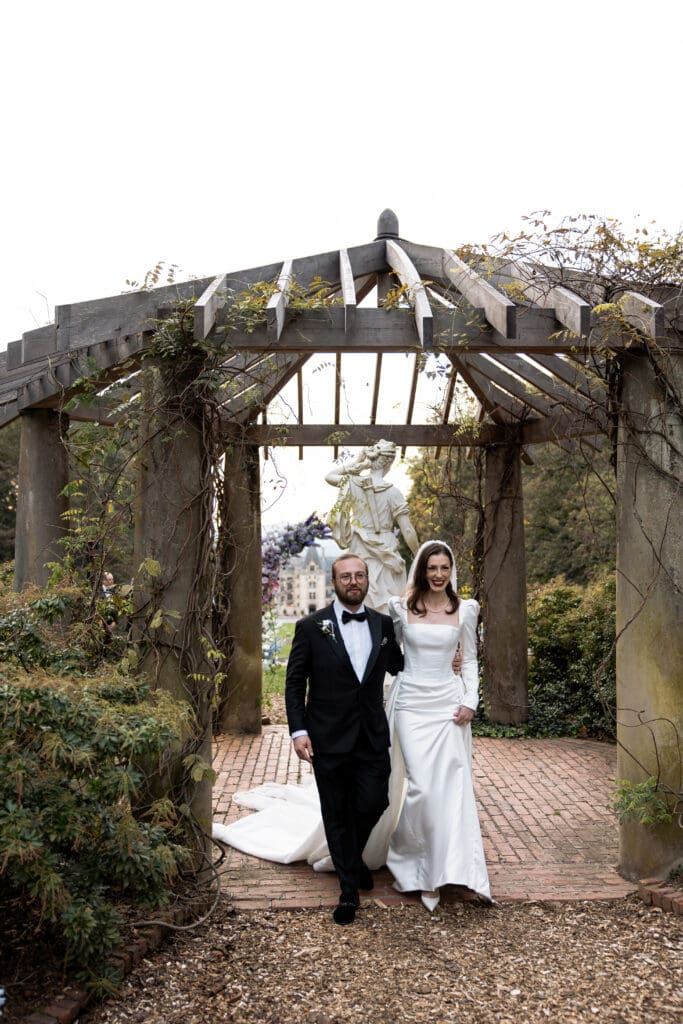 Bride walking arm-in-arm with her father under a stone pergola at the Biltmore Estate before the ceremony, featured in Biltmore wedding photos.