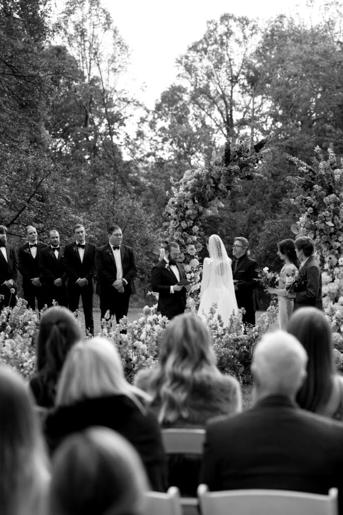 Black-and-white ceremony moment facing the floral arch at the Biltmore Estate, captured by a Biltmore wedding photographer.