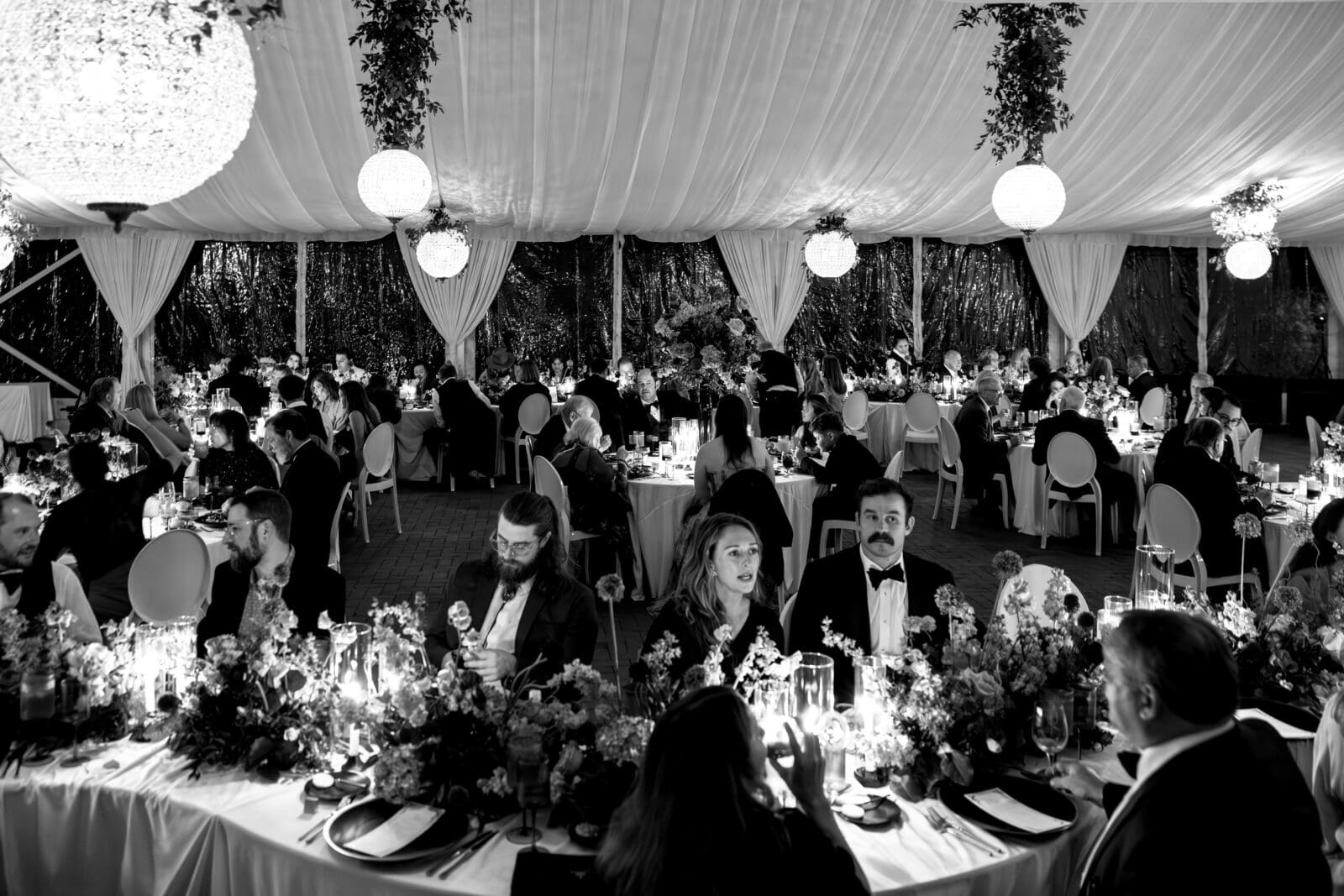 Black-and-white overview of the Biltmore Estate wedding reception with candlelit tables, hanging lanterns, and guests enjoying the evening.