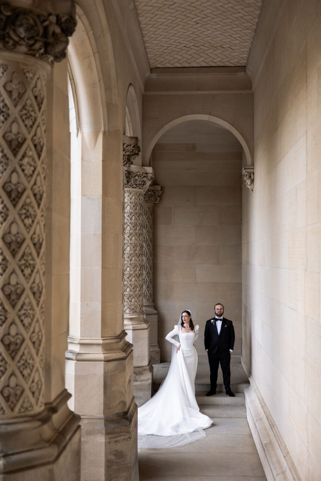 Editorial wedding portrait of the bride and groom standing in the tall stone archways of the Biltmore Estate, showcasing the estate’s architectural detail.