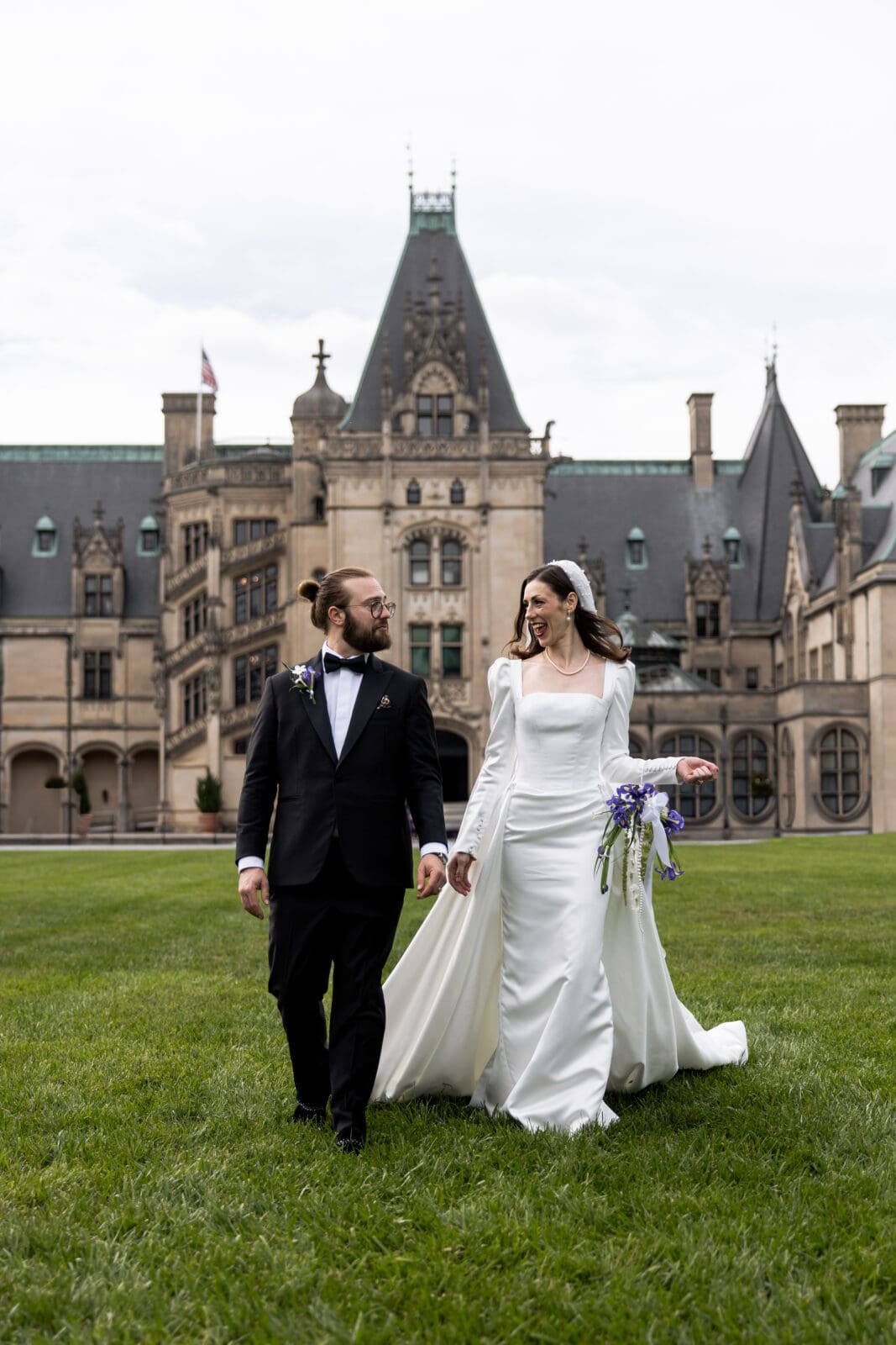 Bride and groom smiling while walking across the lawn at the Biltmore Estate, captured as part of luxury Biltmore wedding photos.