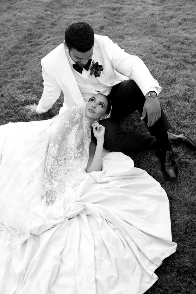 Black and white portrait of bride reclining in her gown beside groom.