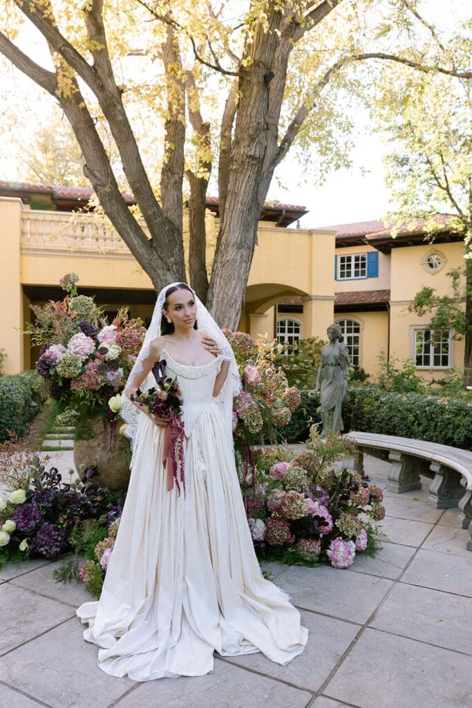 Bride in custom gown holding bouquet in the courtyard at Oceana’s Gardens in Boulder, Colorado.