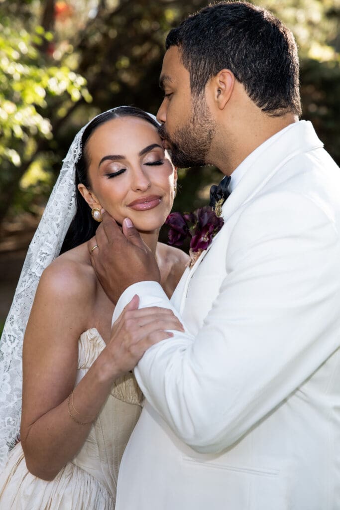 Groom kissing bride’s forehead during golden hour portrait at Oceana’s Gardens.
