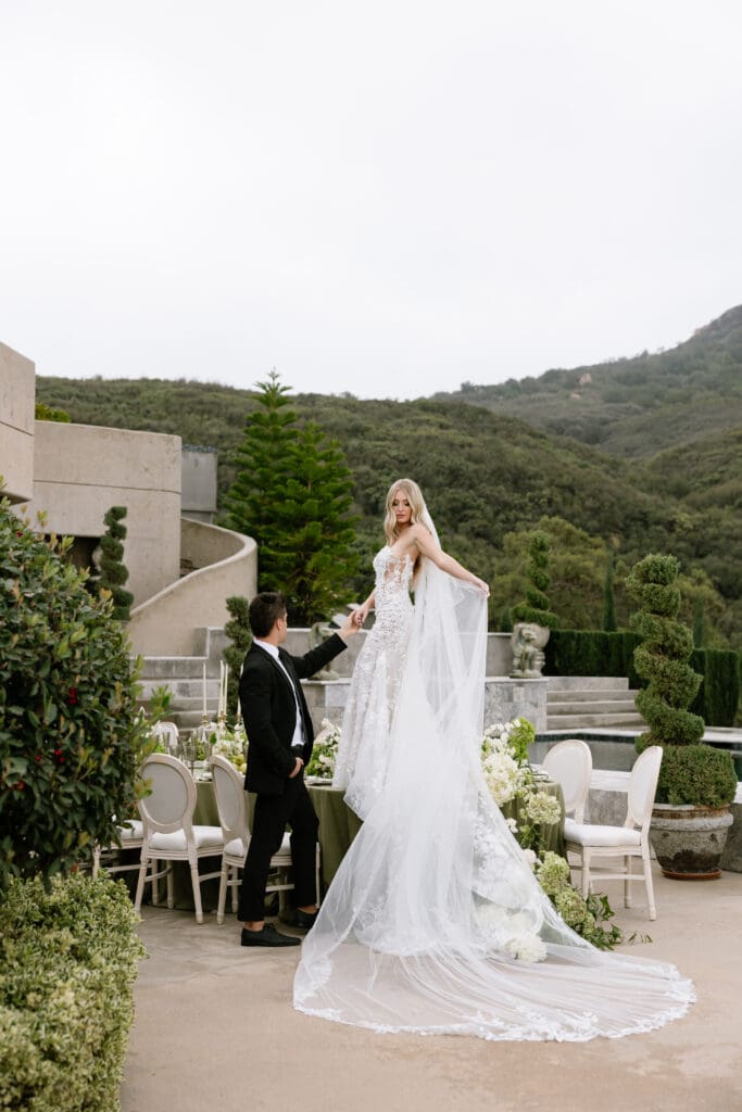 Bride in couture gown with cathedral-length veil standing above an elegant tablescape during a luxury Stone Mountain Estate wedding.