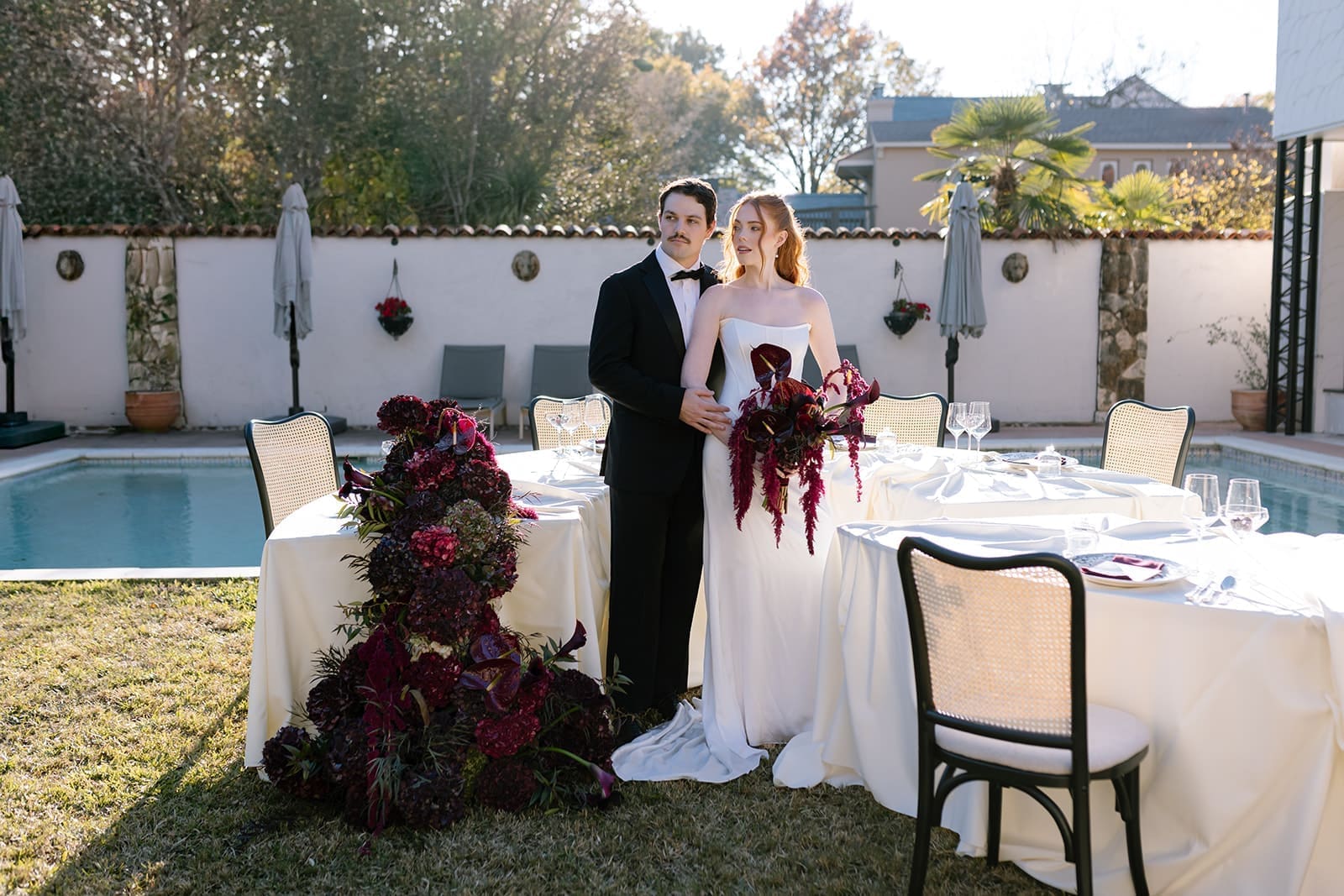 Bride and groom posing at outdoor poolside wedding reception with elegant tables and florals in California.