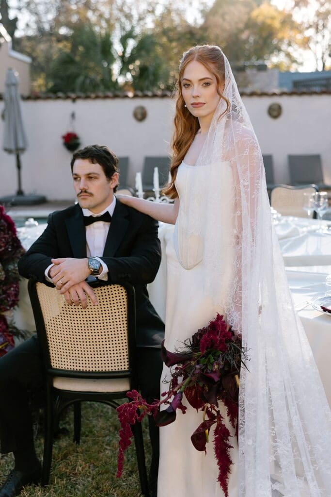 Bride standing behind seated groom during outdoor editorial wedding portrait at a California estate in Santa Barbara.