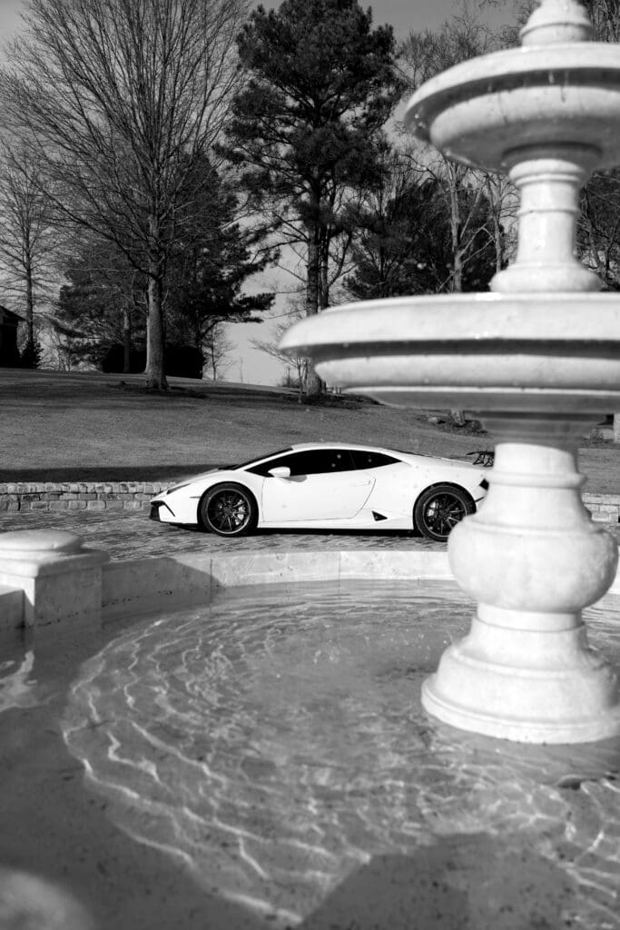 Luxury black and white portrait of a white supercar parked beside a stone fountain at Stone Haven wedding venue in Alabama, photographed with editorial contrast and dramatic light.