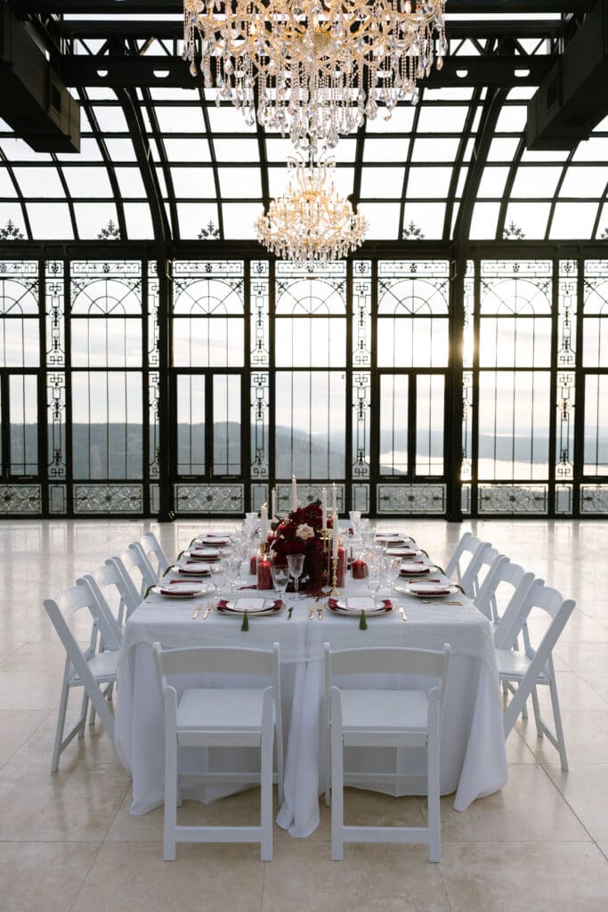 Luxury reception table design with deep red florals, gold settings, and candlelight inside the glass conservatory at Stone Haven wedding venue in Alabama.