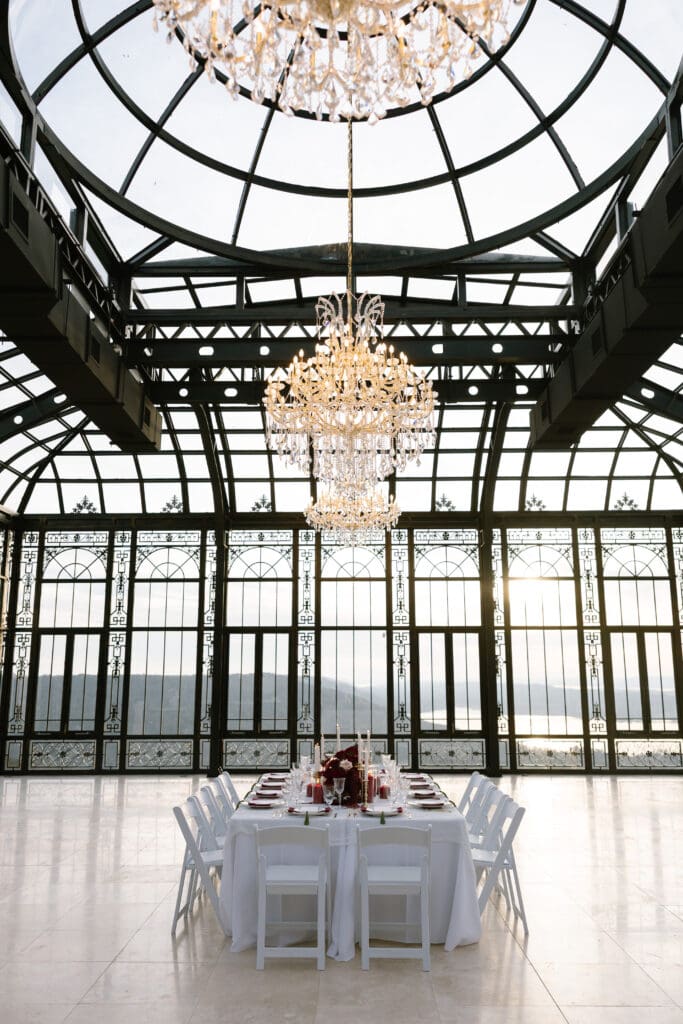 Elegant vertical view of crystal chandeliers above a long luxury wedding reception table inside the conservatory at Stone Haven wedding venue in Alabama.