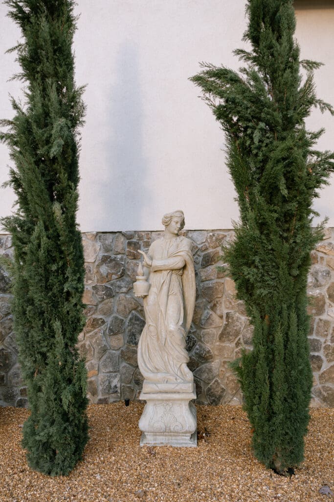 Elegant classical garden statue framed by tall cypress trees at Stone Haven wedding venue in Alabama, styled for a luxury editorial wedding atmosphere.