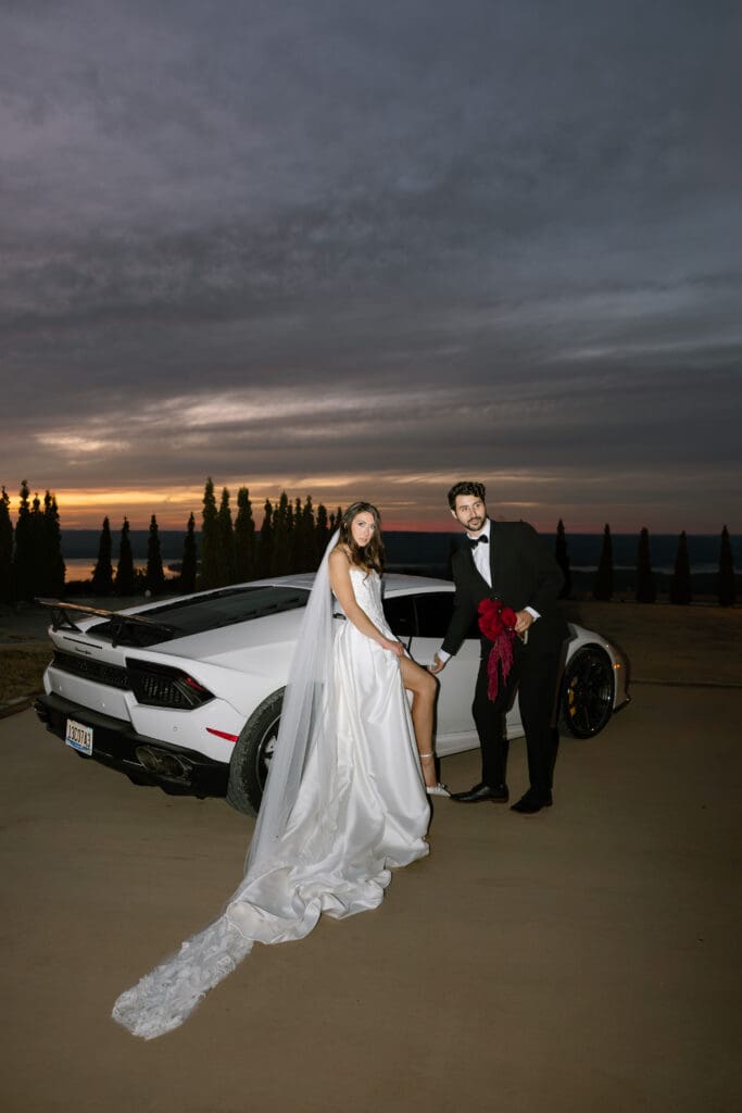 Editorial sunset wedding portrait of bride and groom beside a white supercar overlooking the valley at Stone Haven wedding venue in Alabama with dramatic twilight sky.