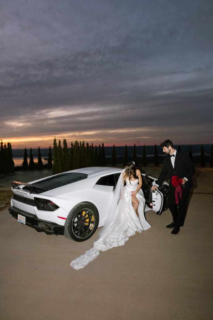 Bride stepping out of a white luxury Lamborghini with cathedral veil and satin gown flowing at sunset at Stone Haven wedding venue in Alabama, photographed by a luxury wedding photographer.