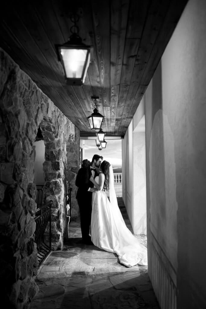 Black and white wedding portrait of bride and groom sharing an intimate kiss beneath lantern lighting along the stone covered walkway at Stone Haven wedding venue in Alabama.