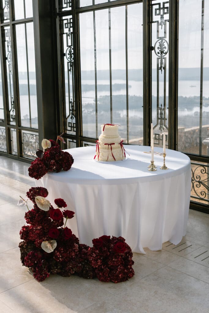 Luxury wedding cake display with deep red florals and gold candlesticks inside the glass conservatory at Stone Haven wedding venue in Alabama, captured with natural light.