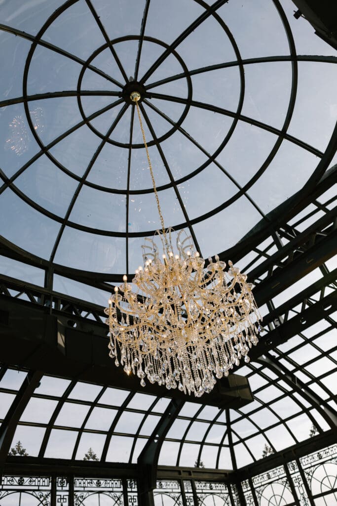 Crystal chandelier hanging beneath the curved glass ceiling inside the grand conservatory at Stone Haven wedding venue in Alabama during an editorial wedding shoot.