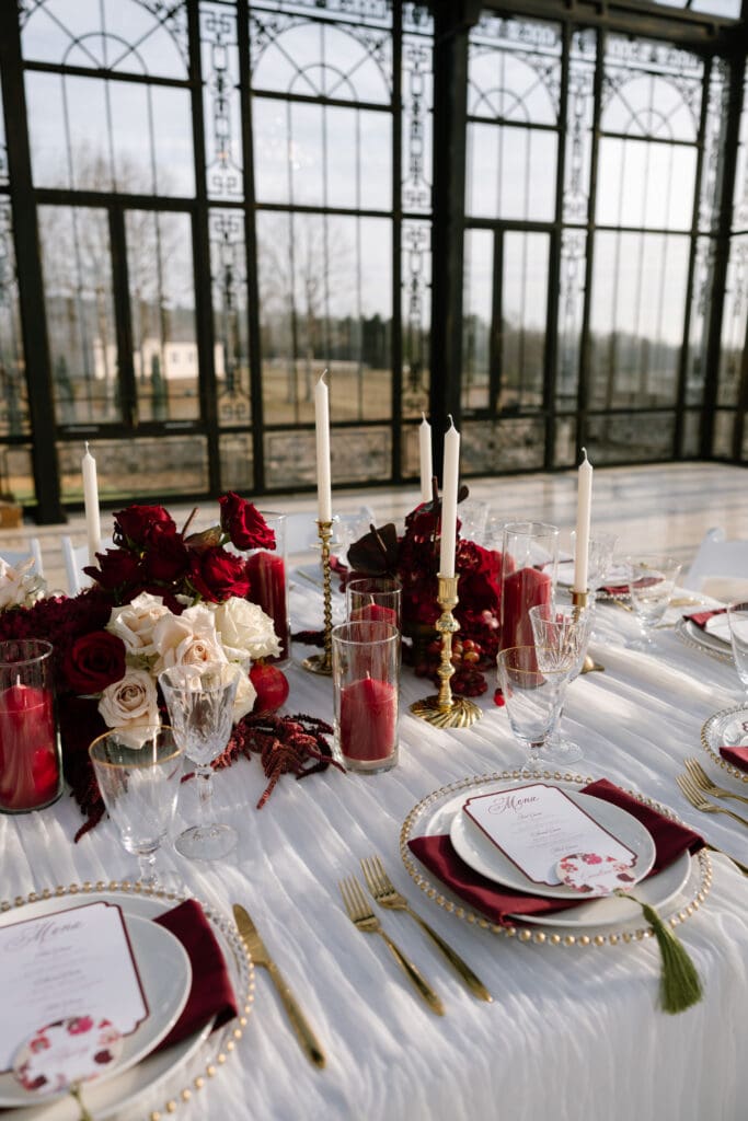 Luxurious reception tablescape with deep red florals, gold candlesticks, and candlelight inside Stone Haven wedding venue in Alabama captured for editorial wedding inspiration.