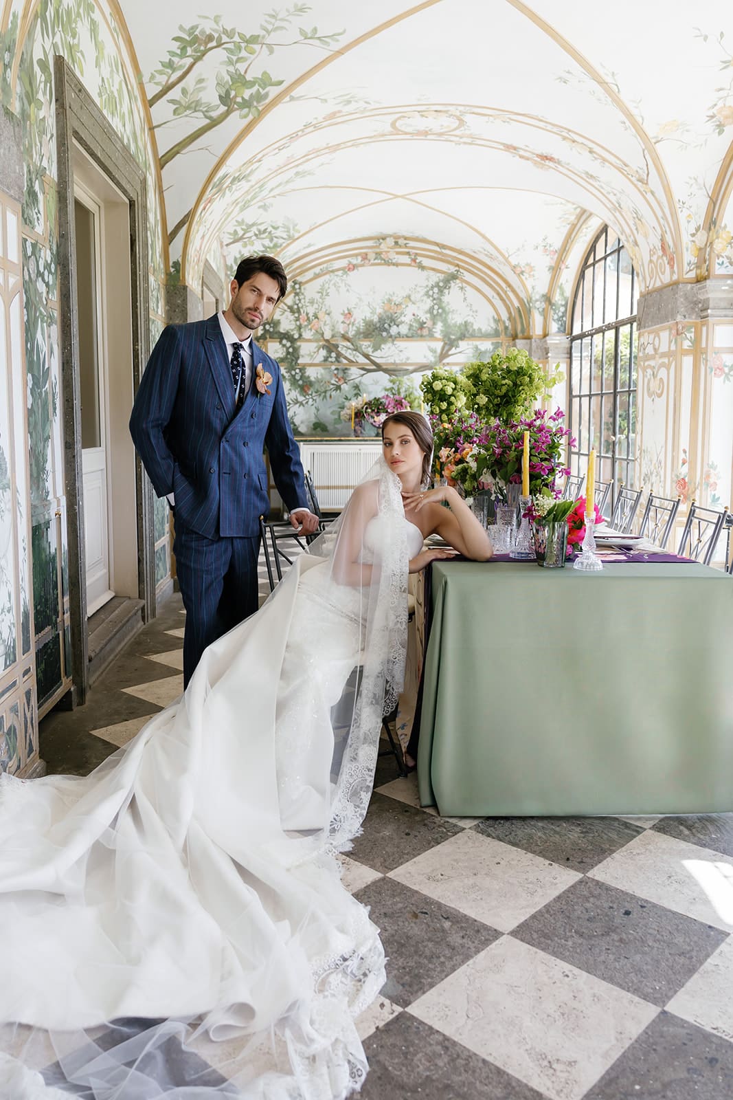 Groom and bride in classical Rome wedding venue with botanical wallpaper, bride wearing flowing lace gown and groom in navy suit, luxury destination wedding photography