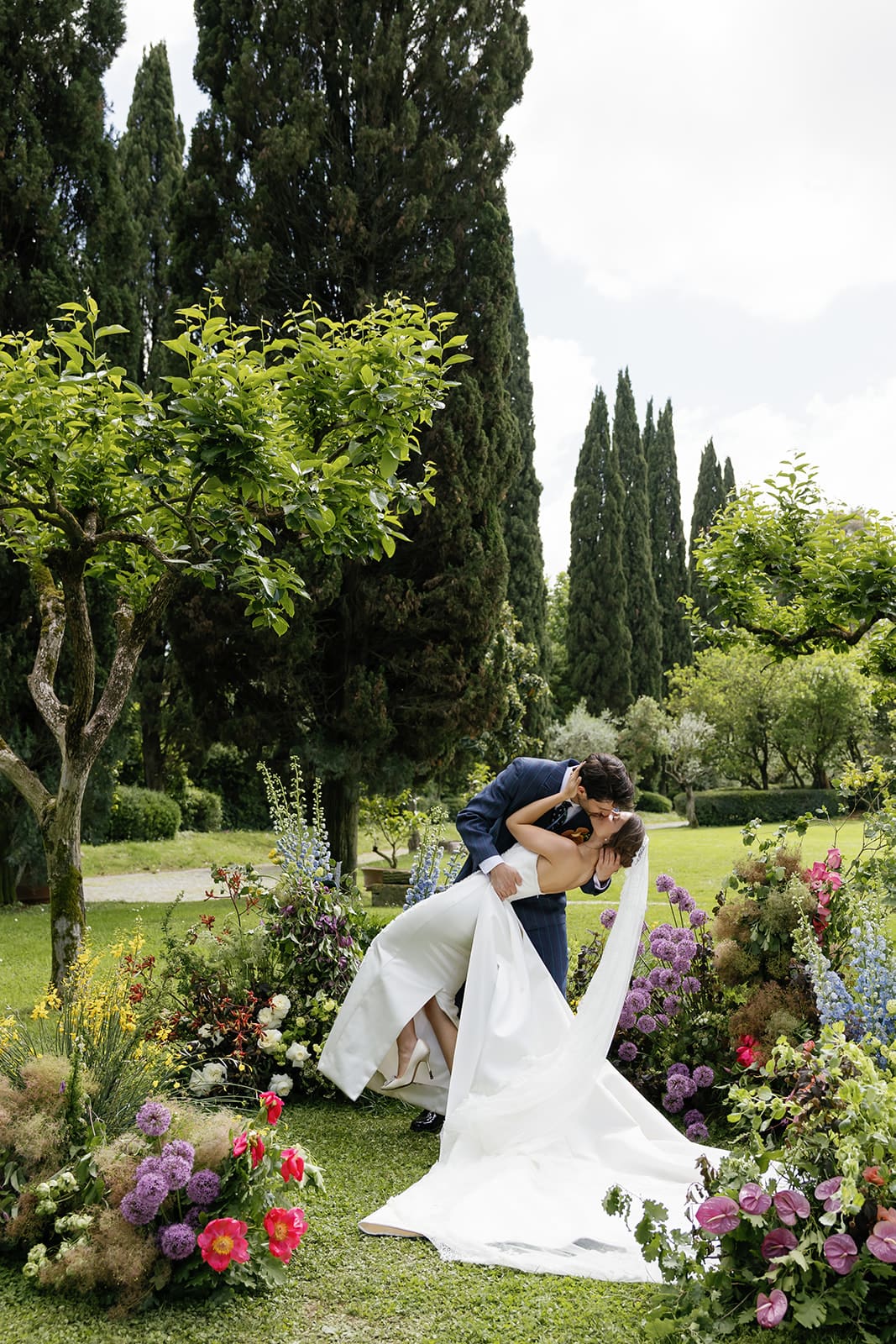 Bride in white wedding gown with flowing train posed among cypress trees and garden flowers at Relais Appia Antica, luxury Rome destination wedding photography