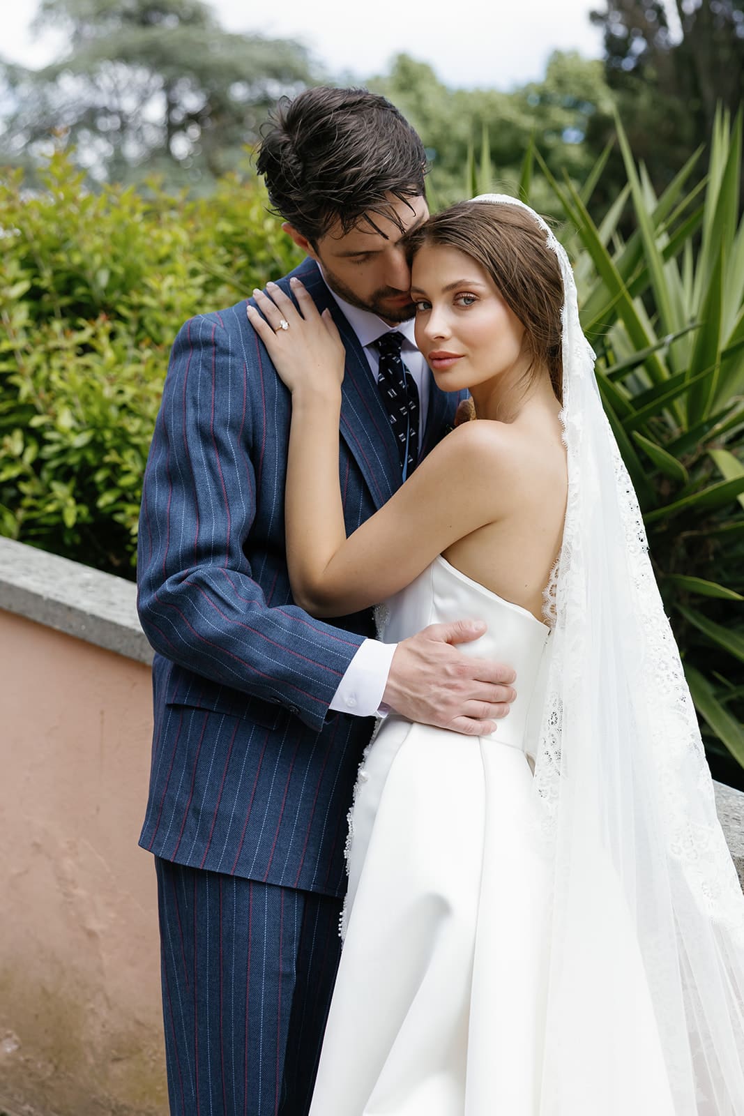 Groom in navy pinstriped suit and bride in white flowing gown with veil, intimate couple portrait at luxury Rome destination wedding, editorial wedding photography