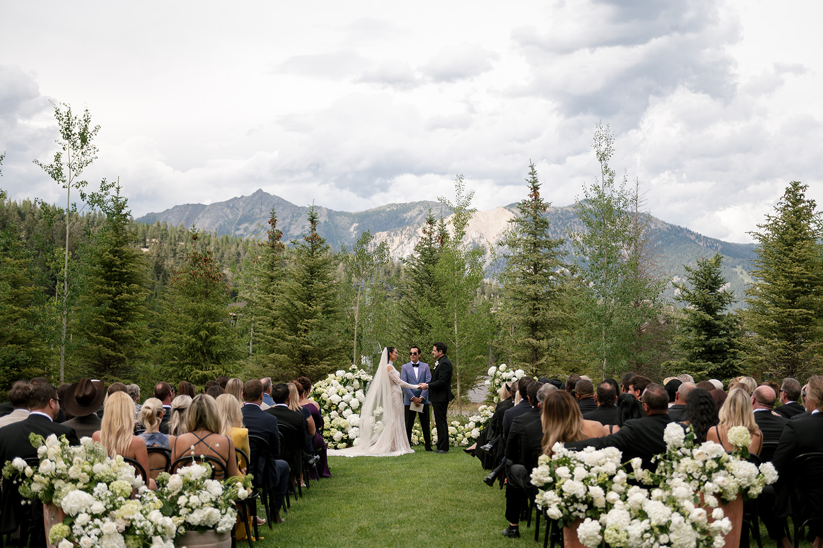Outdoor wedding ceremony at Montage Big Sky with bride, groom, and officiant framed by white hydrangea florals and the Spanish Peaks