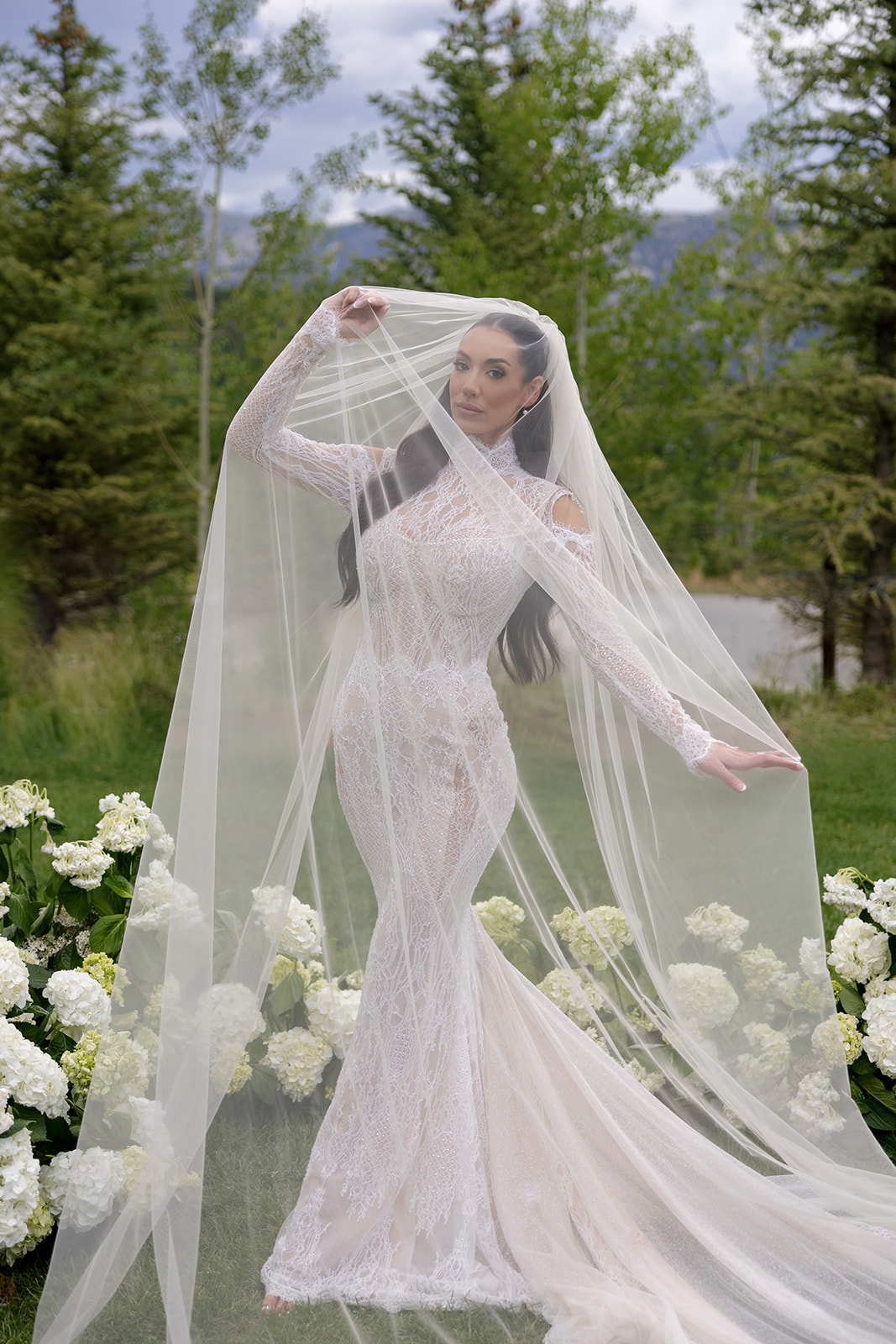 Bride in Galia Lahav Élysée lace gown with cathedral veil at Montage Big Sky, framed by white hydrangea and pine trees