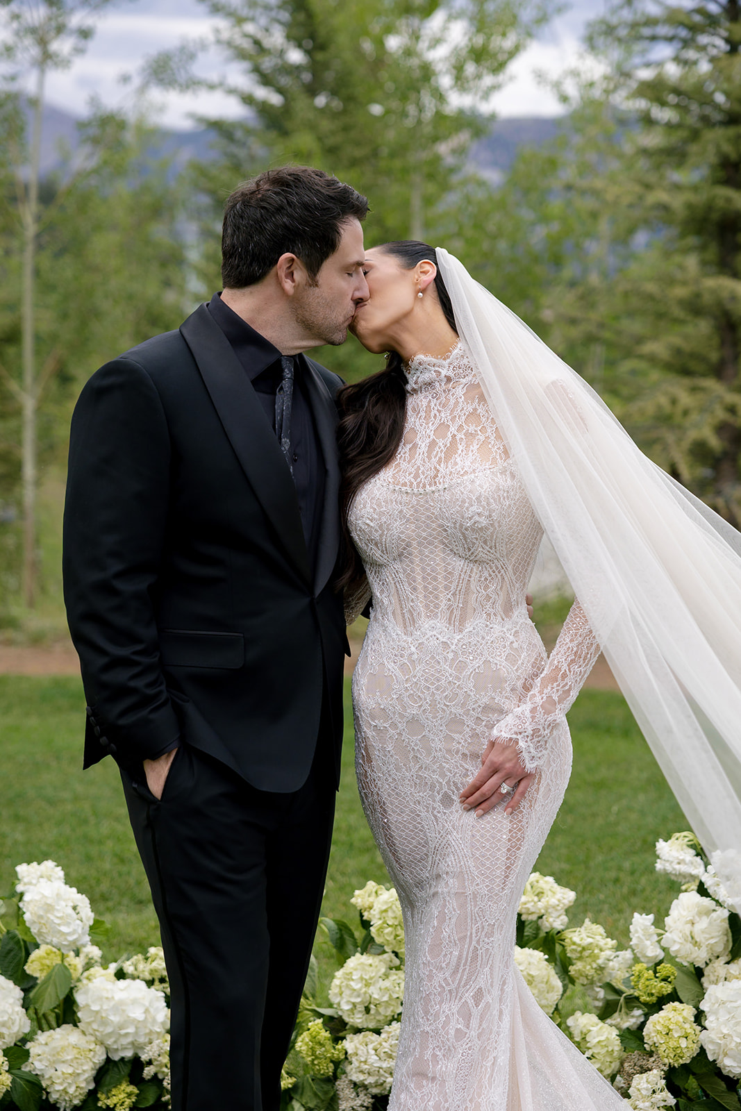 Bride and groom kiss at Montage Big Sky, bride in a Galia Lahav Élysée lace gown with white hydrangea florals and mountains behind them