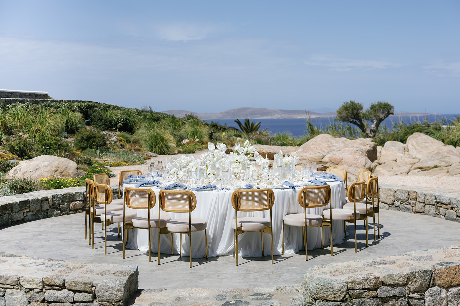 Elegant outdoor wedding reception with blue and white tablescape design surrounded by Mediterranean stone landscaping.