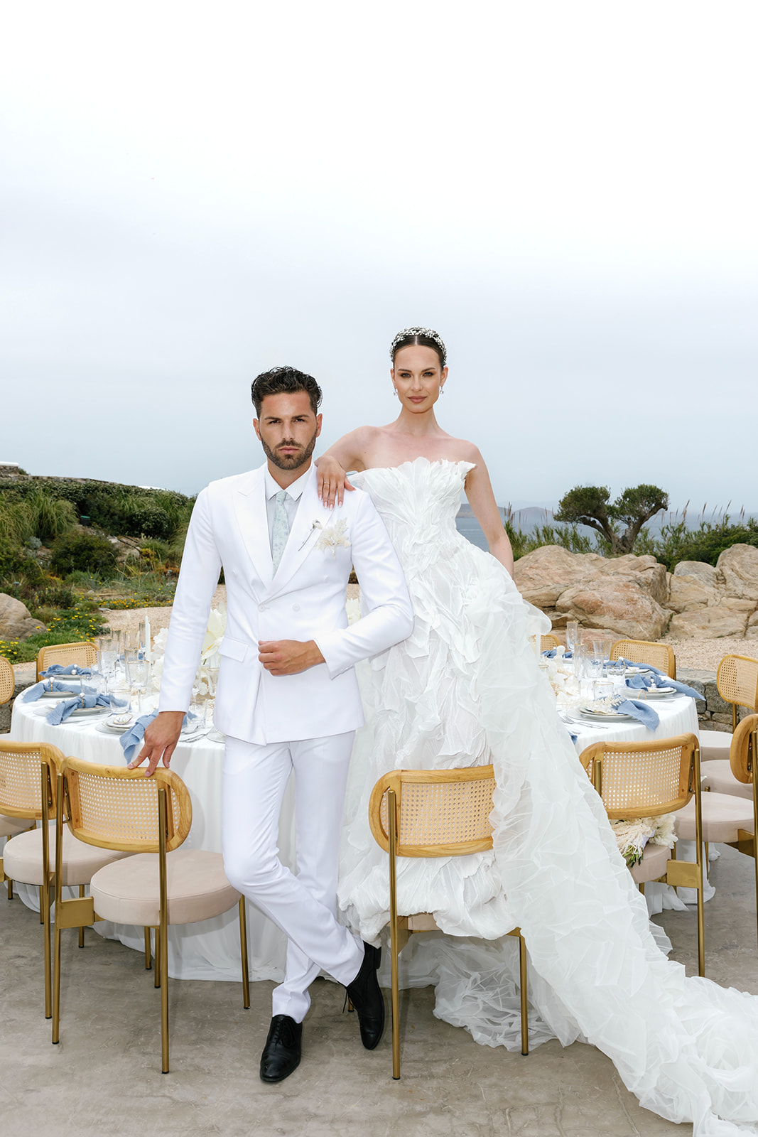 Bride and groom posing together beside an elegant outdoor reception table at a luxury Mykonos wedding.