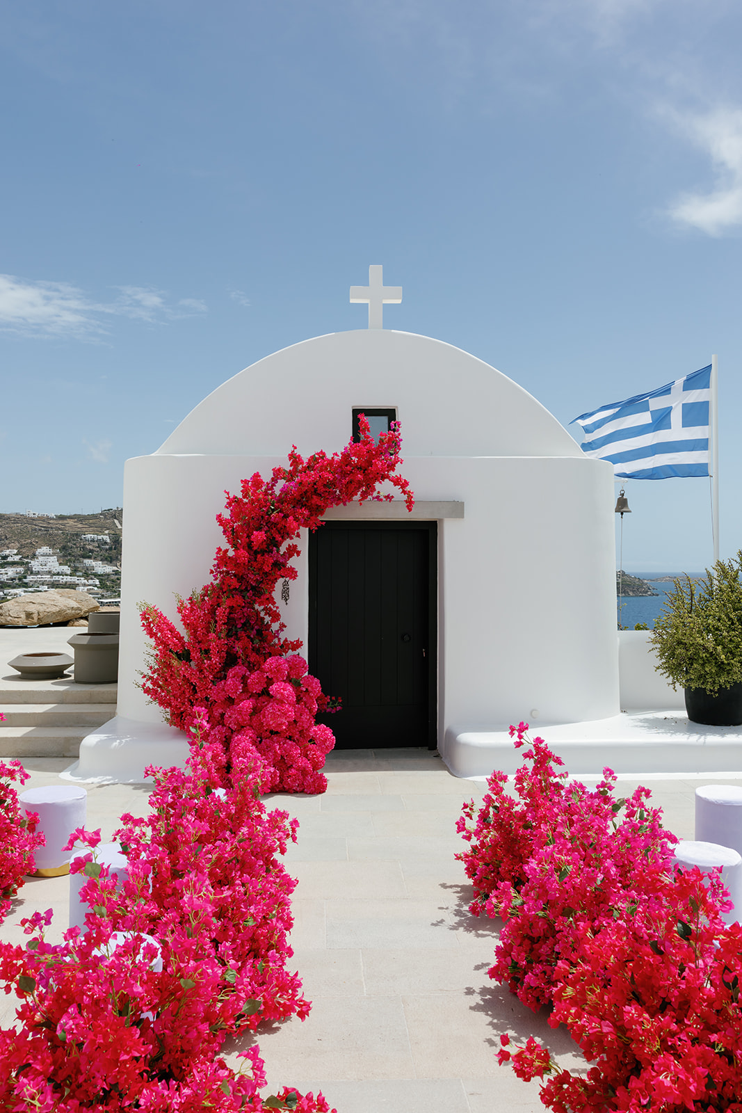 Whitewashed Greek island chapel decorated with vibrant pink florals and a Greek flag at a Kalesma Mykonos wedding.