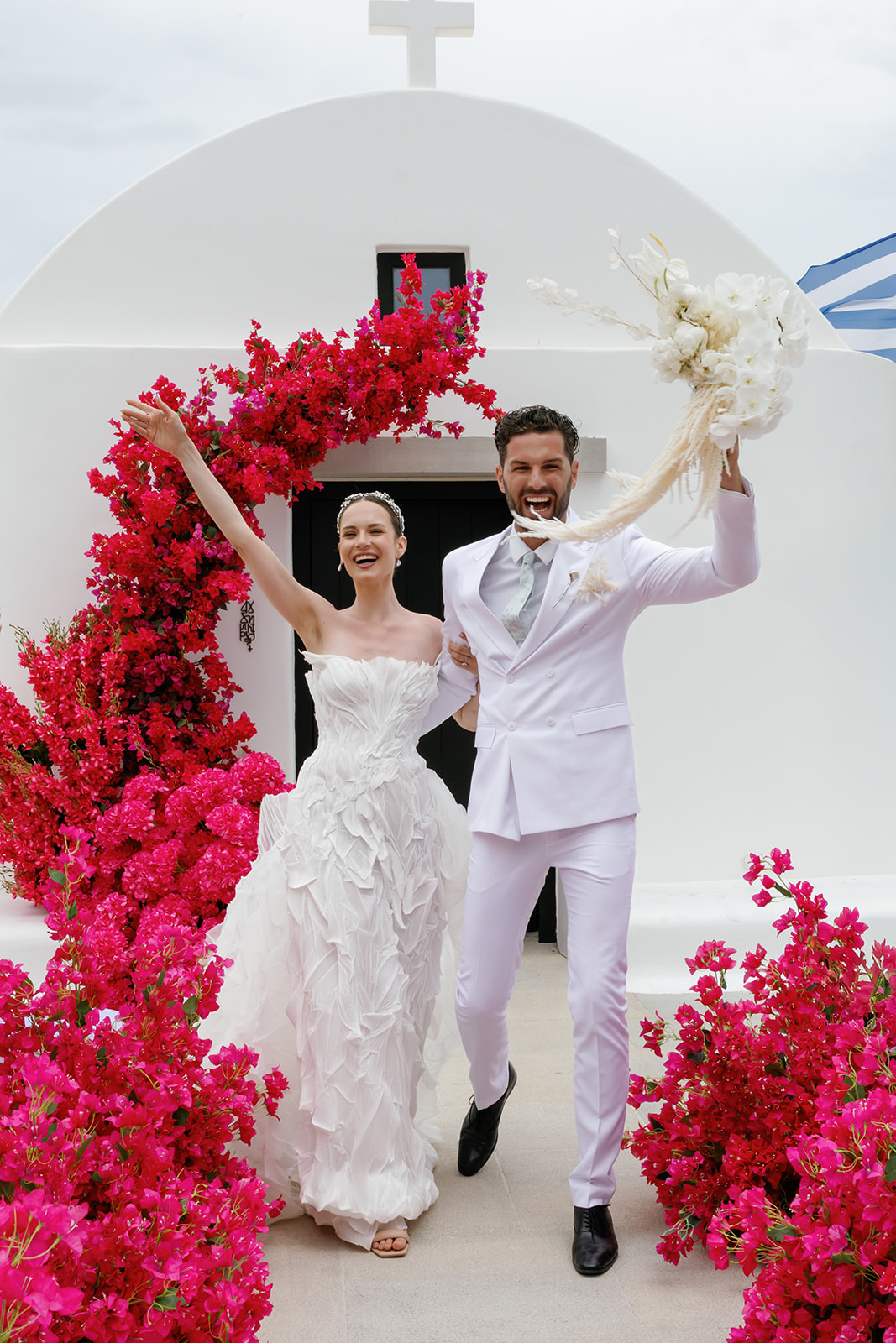 Bride and groom celebrating together beneath a bold pink floral ceremony installation at a luxury wedding in Greece.