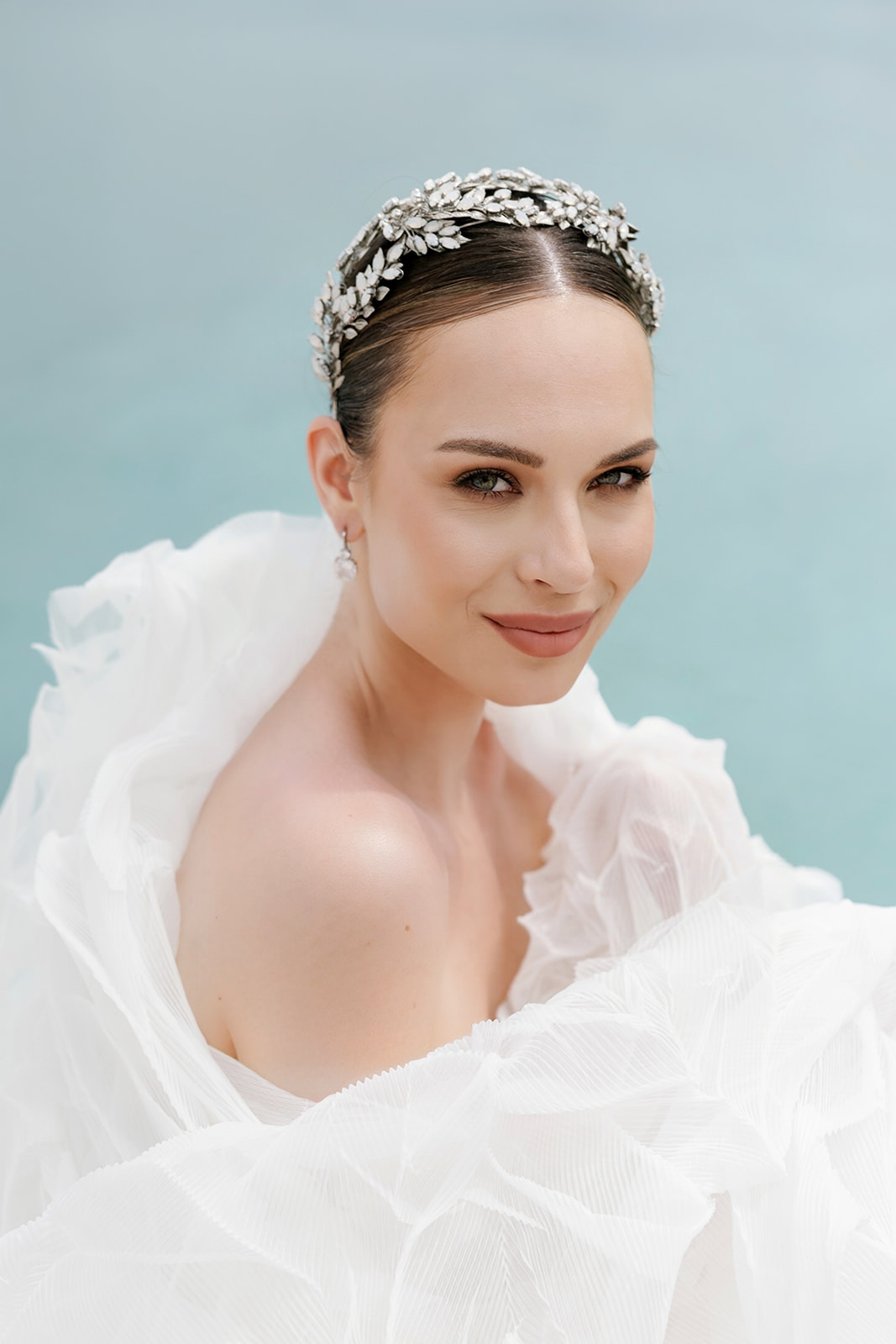 Close up bridal portrait featuring a sleek updo, refined makeup, and statement white floral details at a Mykonos wedding.