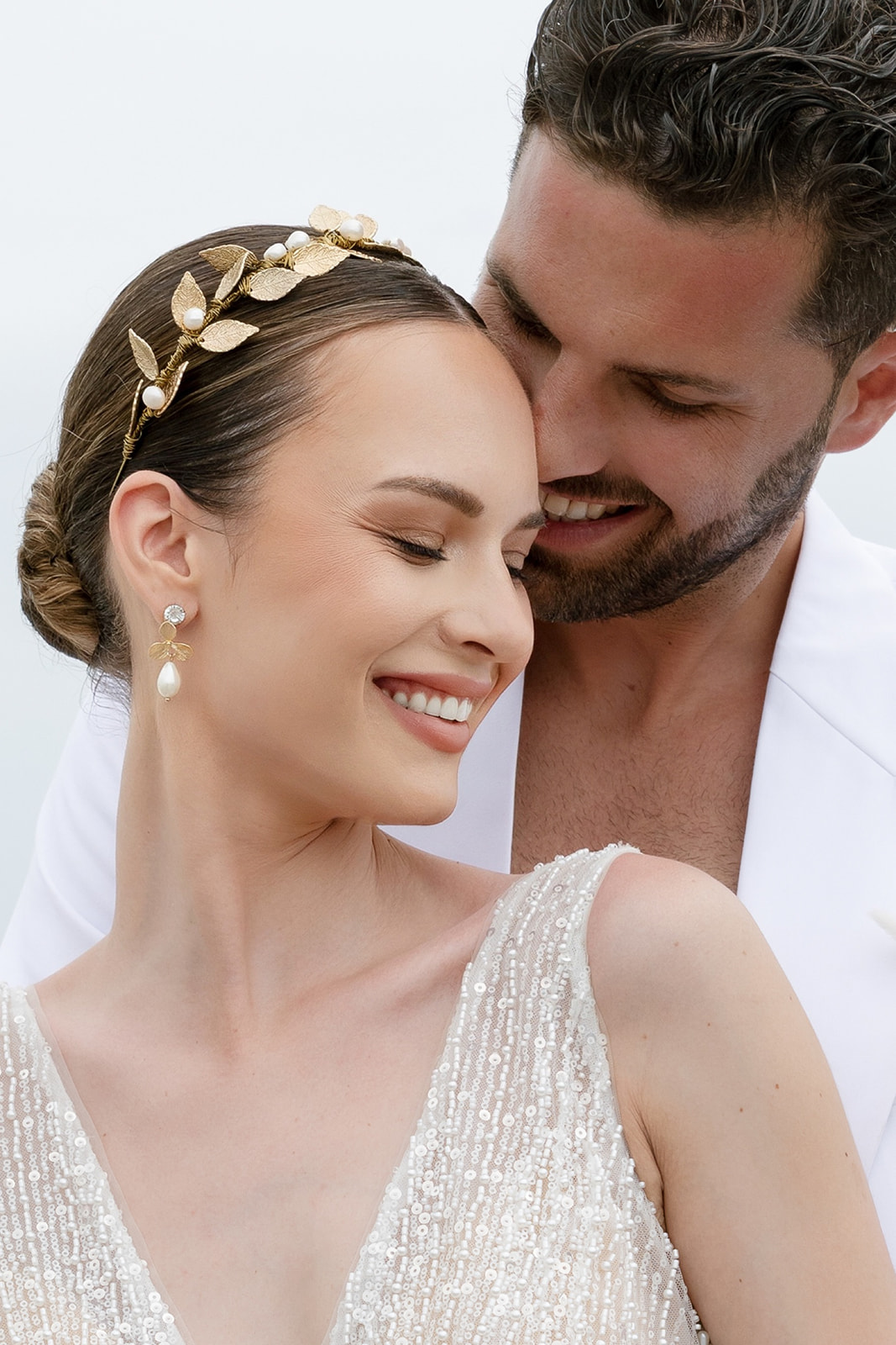 Close up editorial wedding portrait of a bride smiling with her groom against a softly lit Mykonos backdrop.